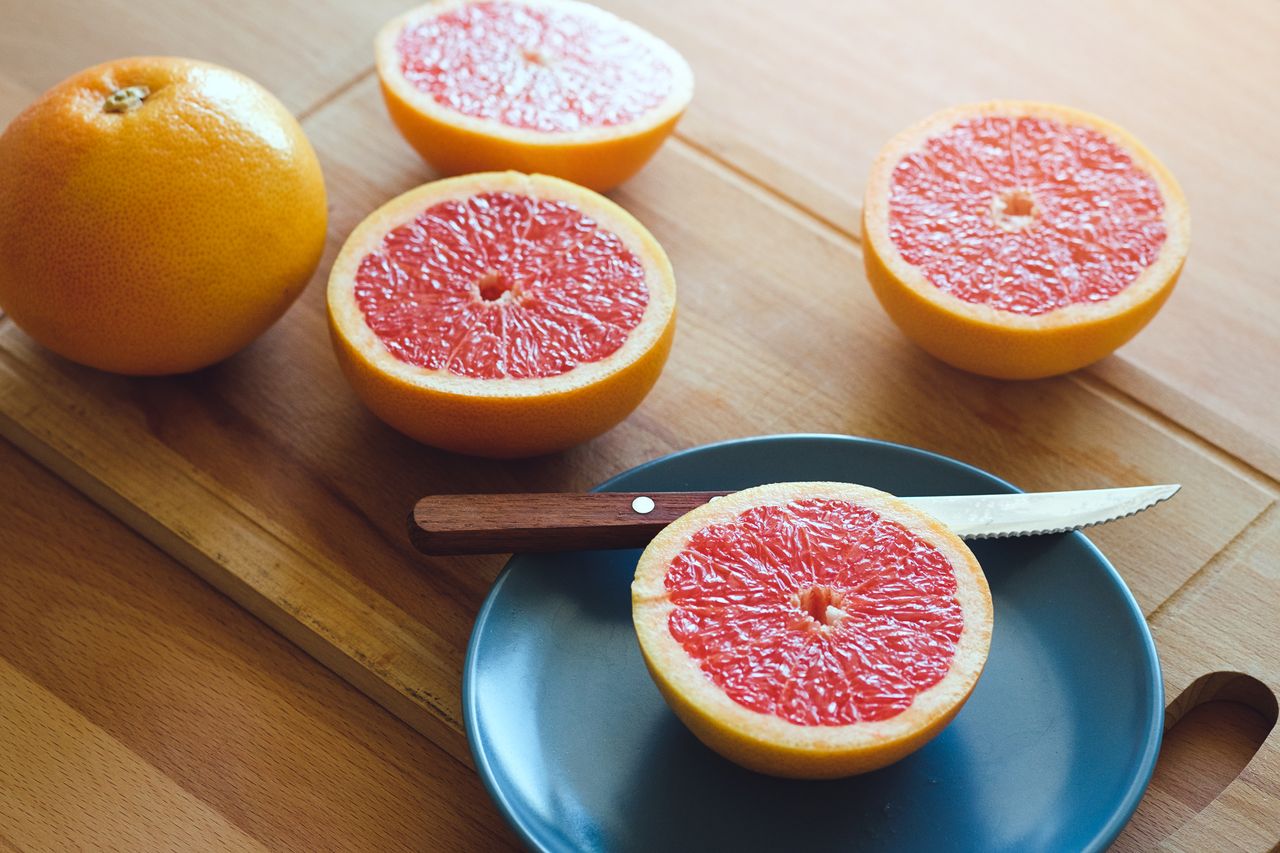 An array of sliced and whole grapefruit, next to a knife and a halved grapefruit on a blue plate, neatly arranged on a wooden table.