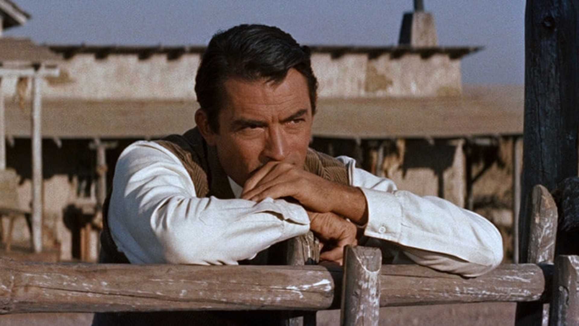 Gregory Peck leans against a fence while thinking in The Big Country