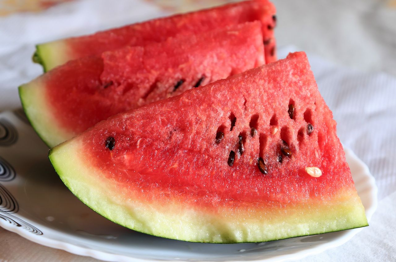 Sliced triangles of fresh watermelon with seeds on a white plate.