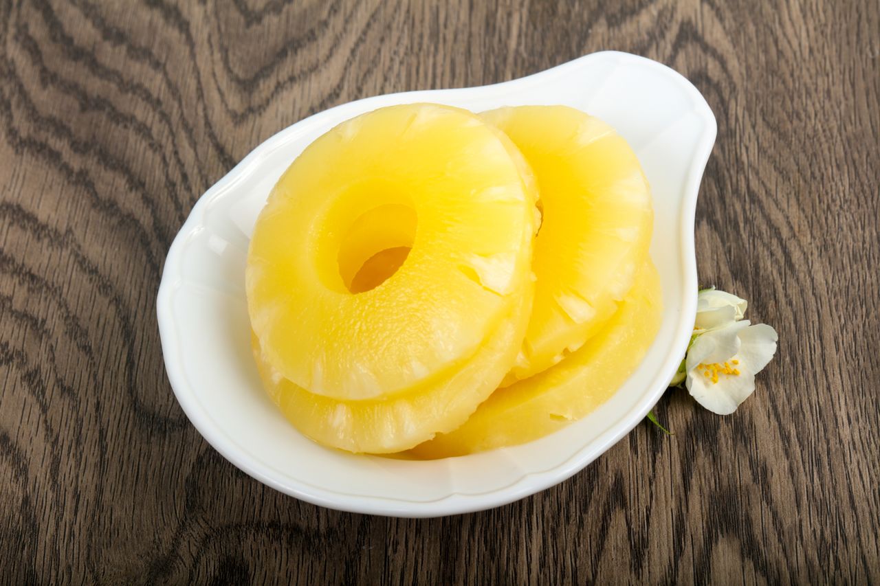 Sliced pineapple rings in a white pear-shaped dish on a wooden table.