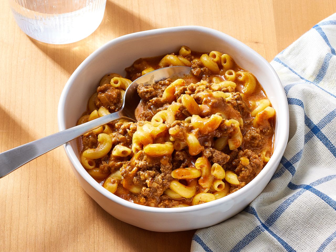 Bowl of macaroni pasta with ground meat and sauce on a wooden table