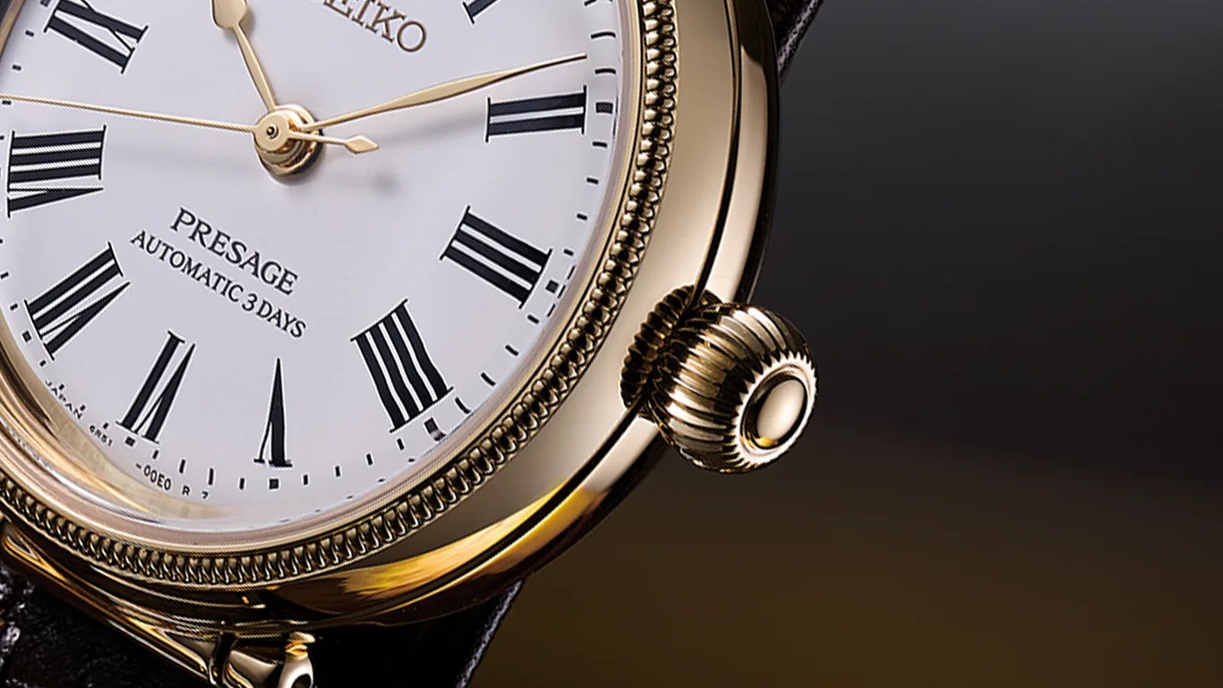 Close-up of a gold-tone Seiko Presage watch with white dial, black Roman numerals, and a ridged crown.
