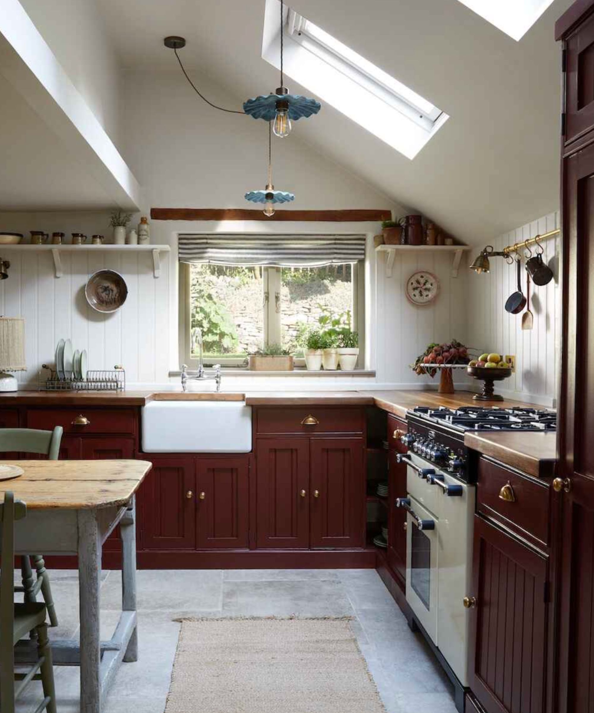 A large kitchen with deep red cabinets, wood countertops, white paneled walls, and a gray freestanding island