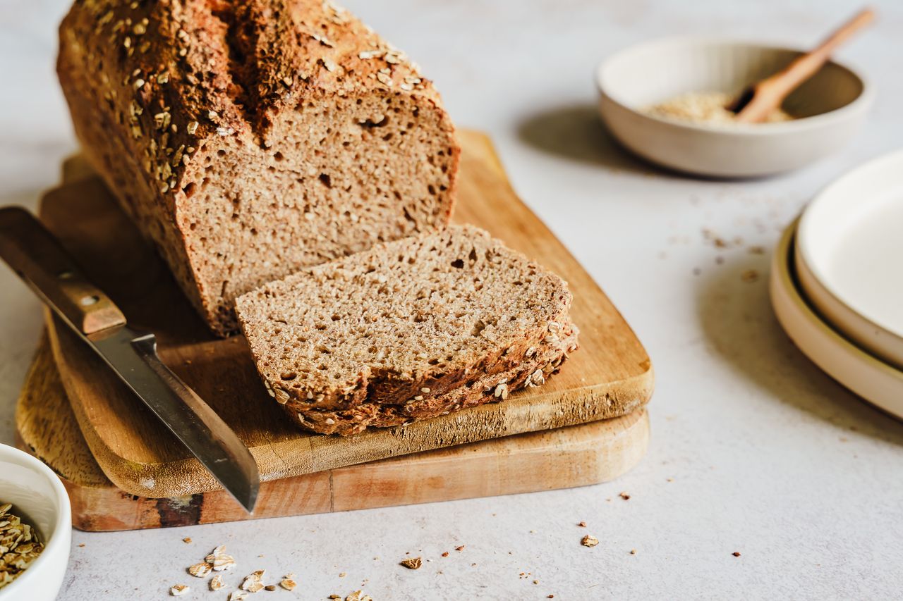 Loaf of whole wheat bread sliced on wooden cutting board next to knife