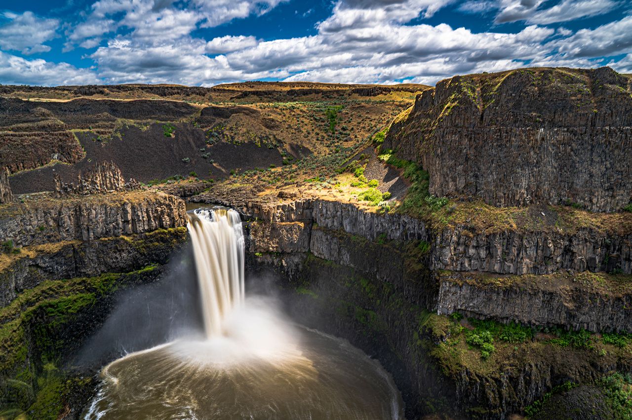 A towering waterfall surrounded by a rocky canyon and open sky