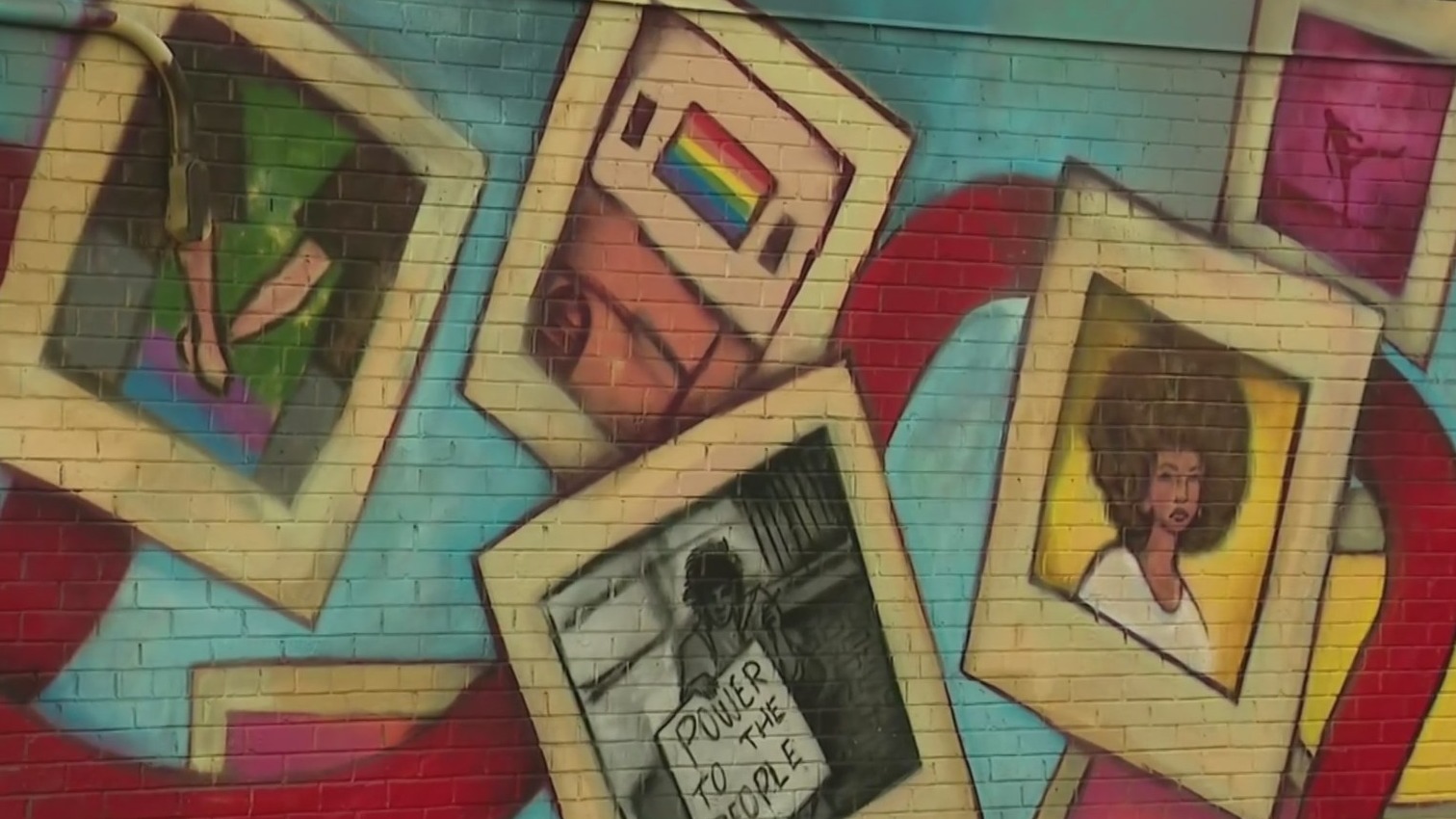 A vibrant mural featuring framed portraits and a slogan on brick wall