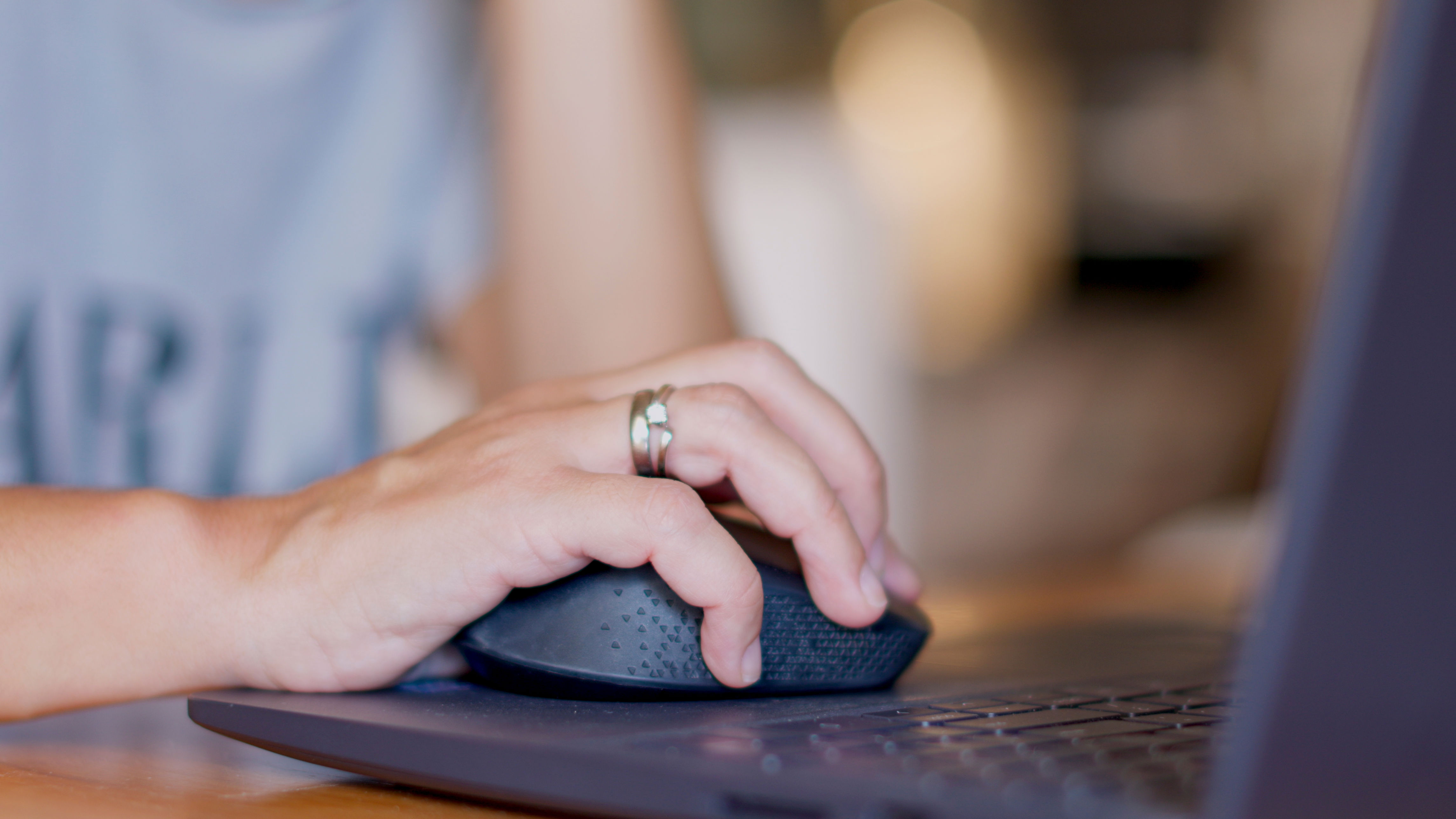 Person using a computer mouse next to a laptop on a desk, partially visible ring on hand