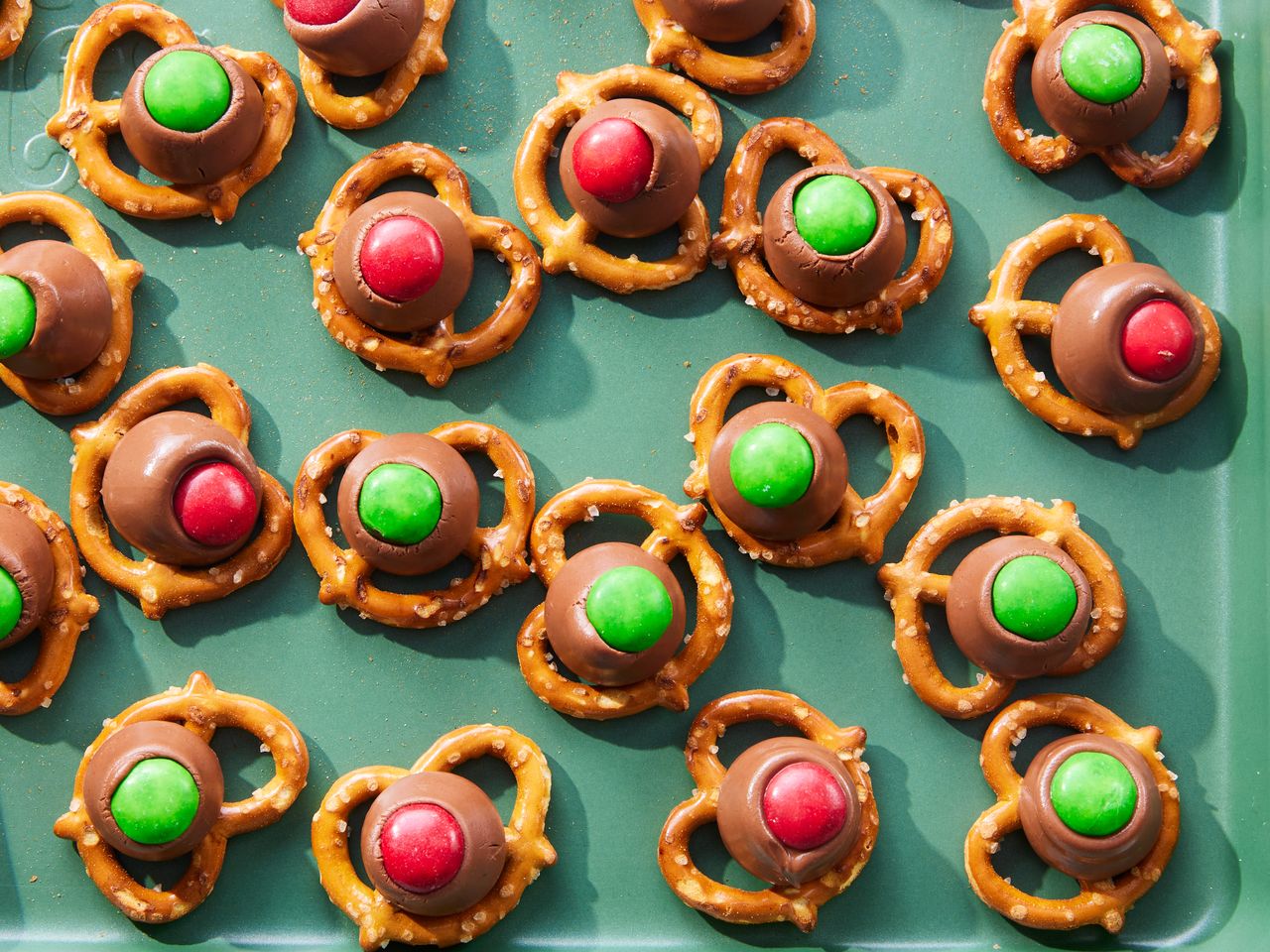 A green platter with chocolate pretzel treats, topped with red and green coated candies