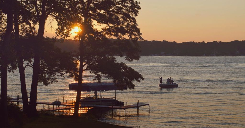 Sunset on a lake with people fishing on a boat in the lake.