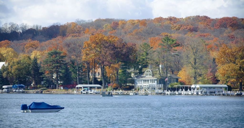 A large lake with a small boat on it with autumn foliage in the background.