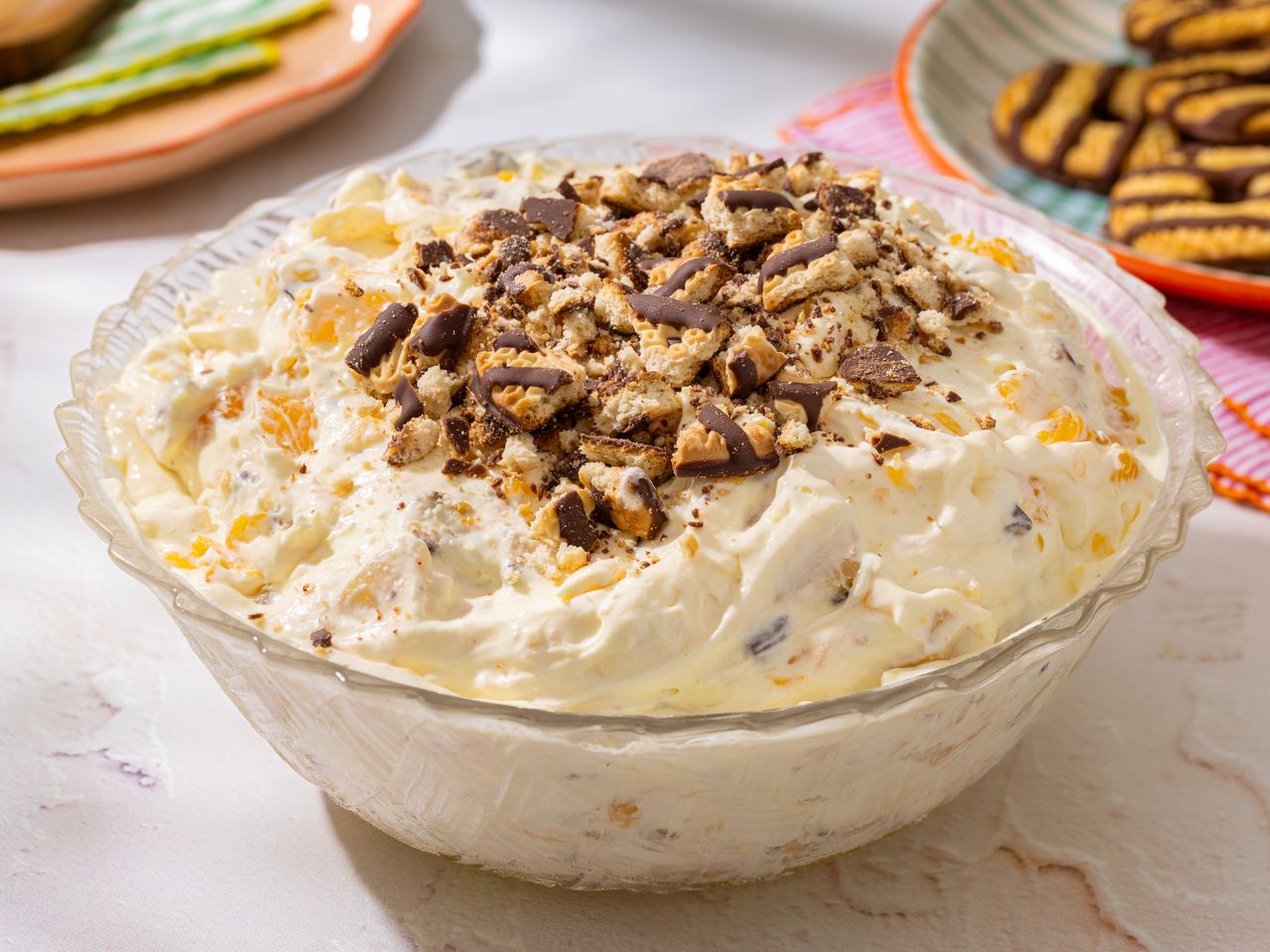 Bowl of dessert salad topped with crushed cookies surrounding plates with cookies visible
