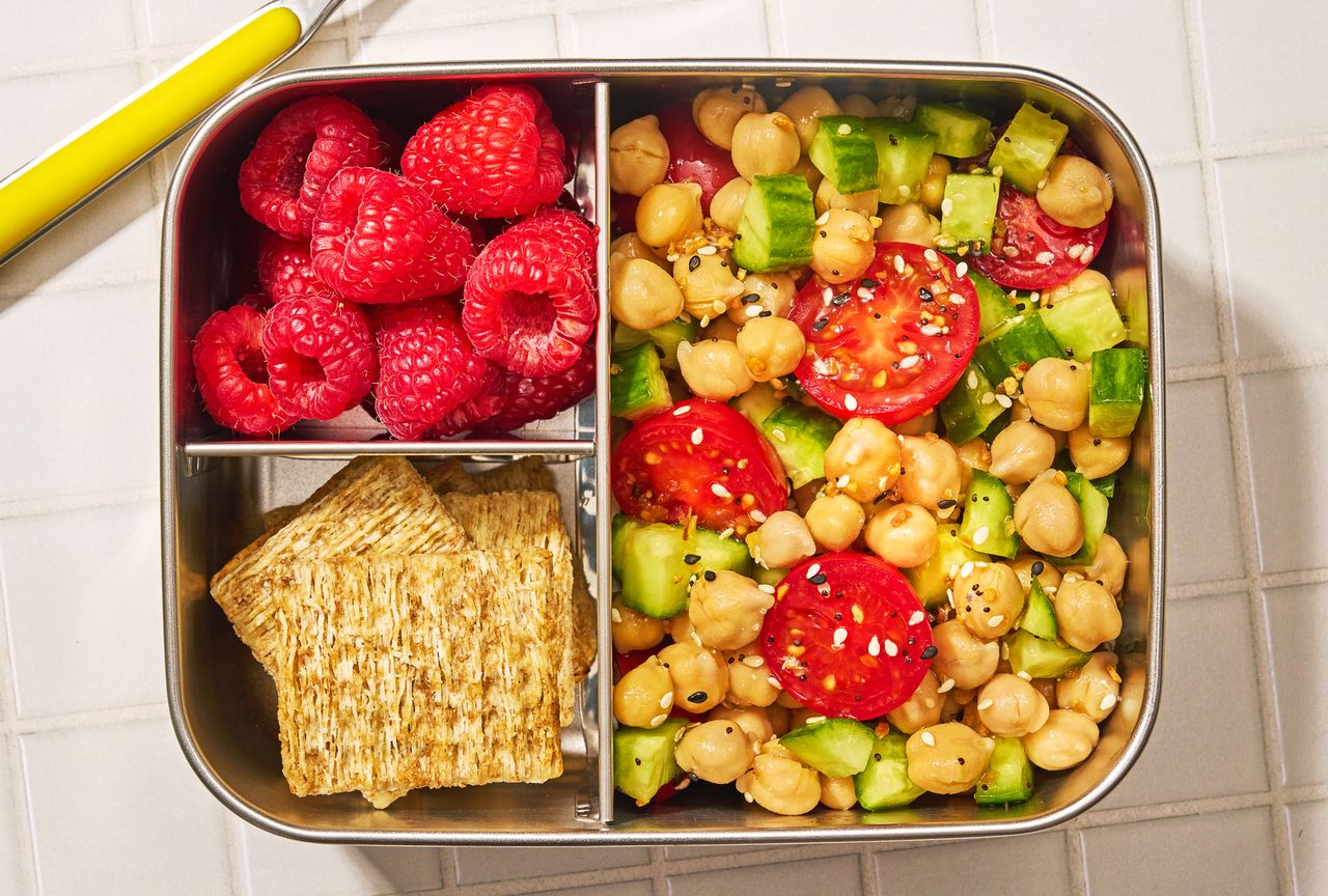 Lunchbox with raspberries crackers and a chickpea salad with cucumbers and tomatoes