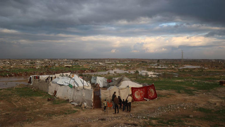 Displaced Palestinians stand outside a tent shelter following heavy rains in the Nuseirat refugee camp, in central Gaza, on December 13. - Eyad Baba/AFP/Getty Images