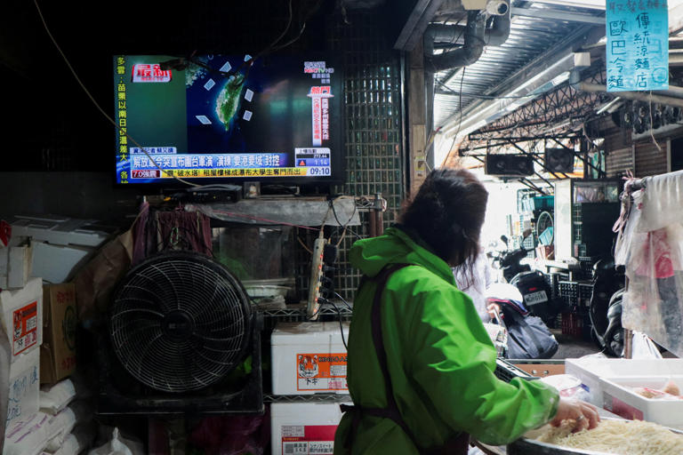A woman works in a noodle store near a television screen in  in Taipei, Taiwan, showing a news report on China's 