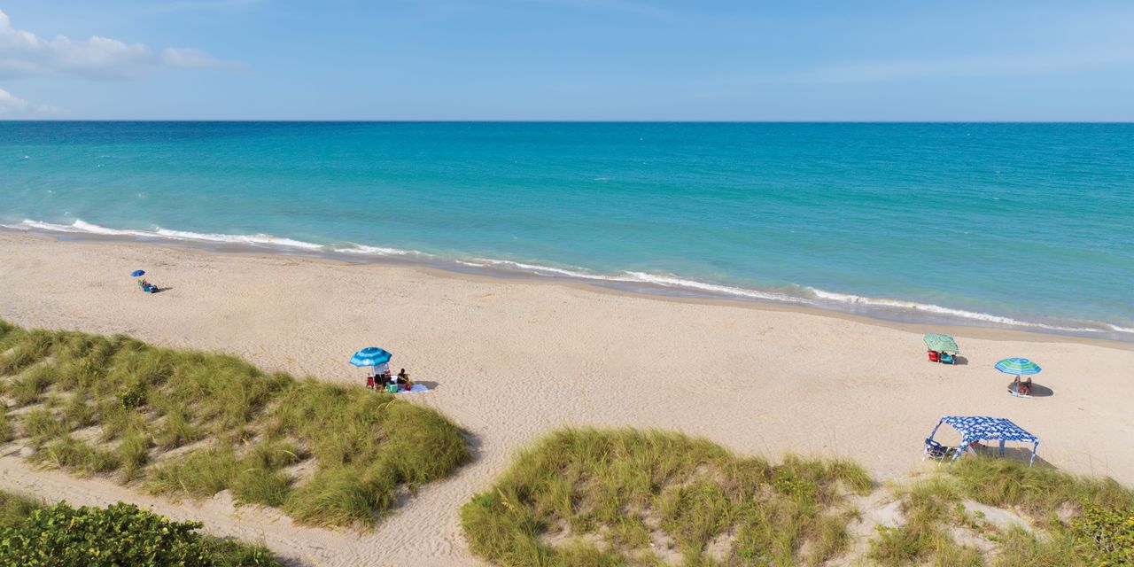 A beach with scattered people under umbrellas ocean and dunes in view