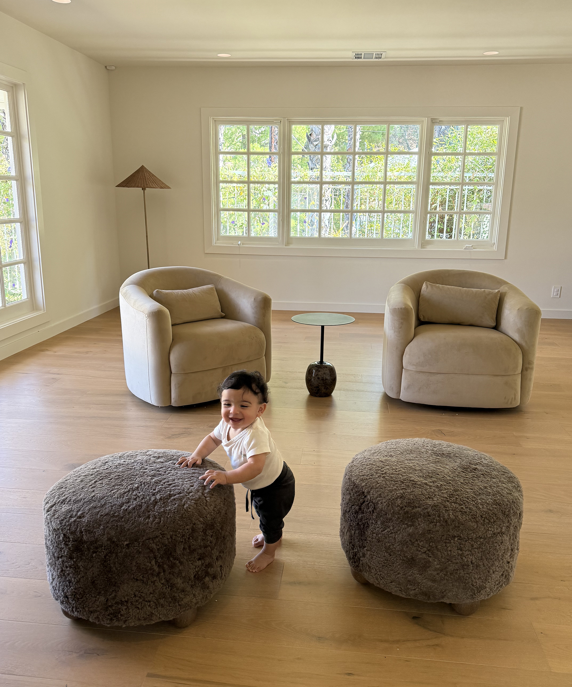 living room mid-decoration with twin armchairs and twin ottomans and a toddler standing up in the middle