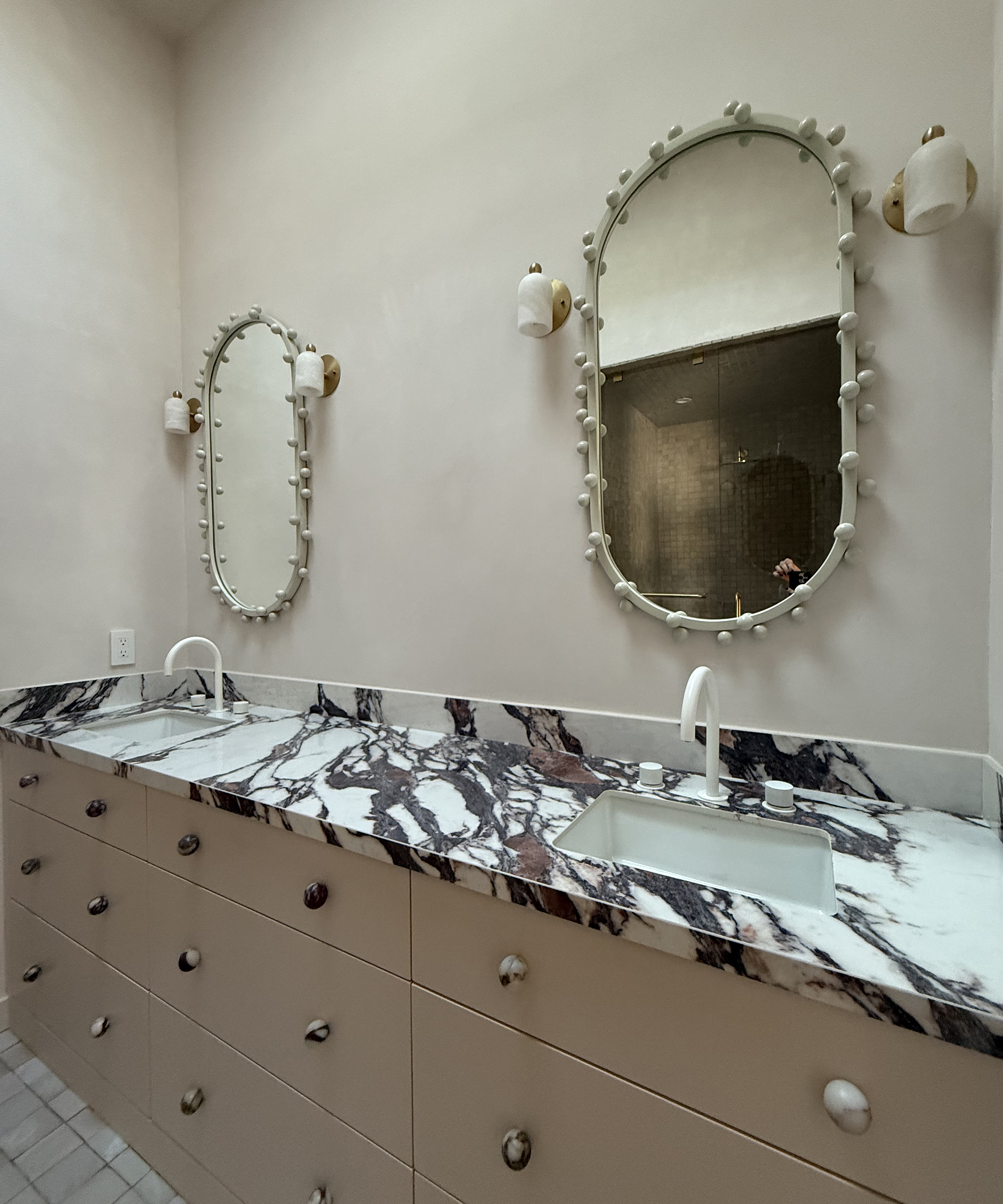 marble-topped bathroom vanity with two oval mirrors on the wall above it