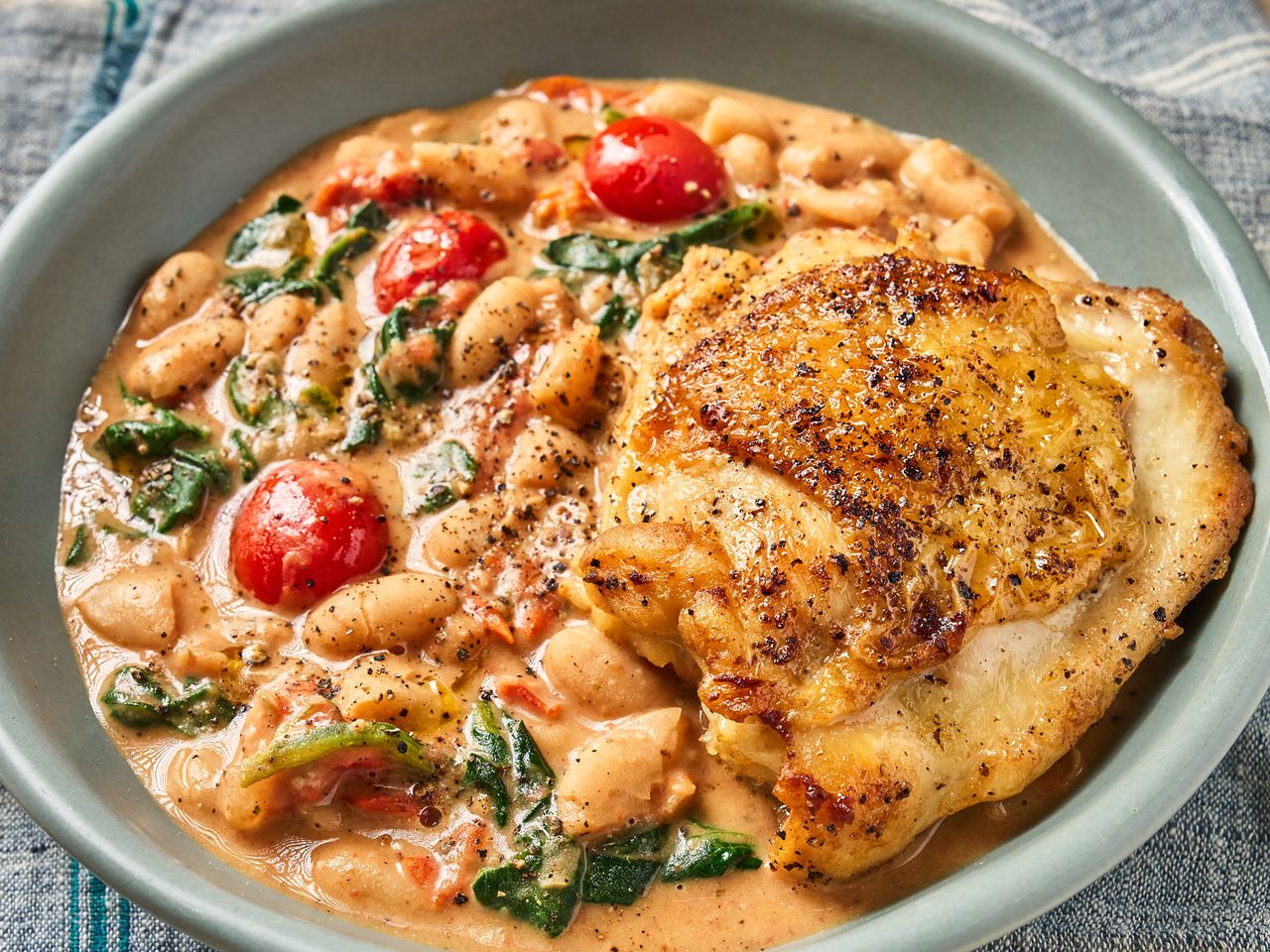 A skillet meal with chicken thigh white beans and vegetables served in a creamy sauce