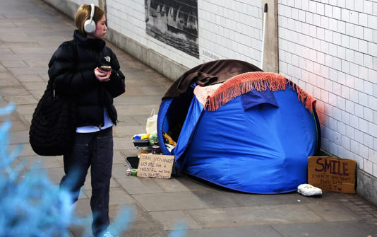 A pedestrian walks past a tent used as shelter by a homeless person in London