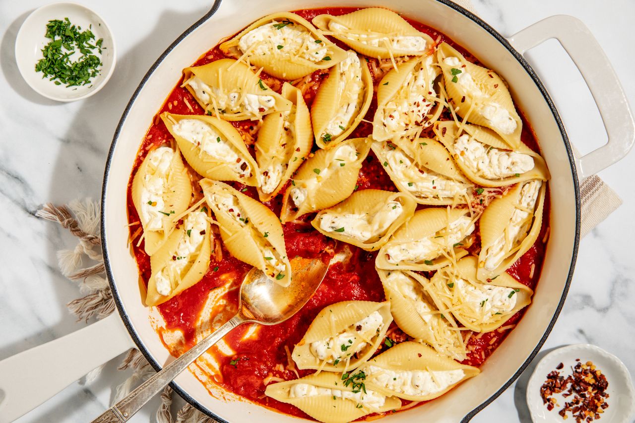 Stovetop Stuffed Shells in a large pan with a large serving spoon - small dish with crushed red pepper and small dish with chopped parsley
