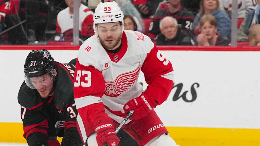 Dec 27, 2025; Raleigh, North Carolina, USA; Detroit Red Wings right wing Alex Debrincat (93) tries to control the puck against the check by Carolina Hurricanes right wing Andrei Svechnikov (37) during the second period at Lenovo Center. | James Guillory-Imagn Images