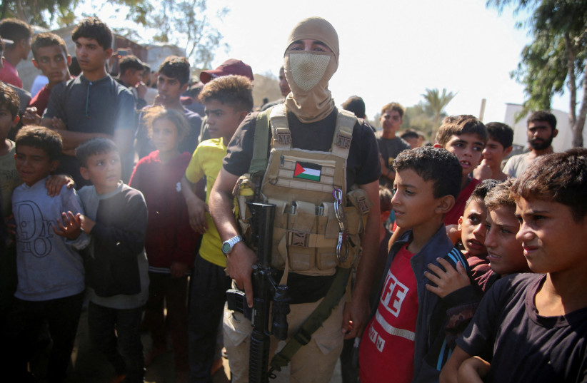 Hamas member stands guard as people gather to watch Red Cross vehicles transporting hostages, following their handover as part of a ceasefire and hostages-prisoners swap deal between Hamas and Israel, in the central Gaza Strip, October 13, 2025. (credit: REUTERS/Stringer TPX IMAGES OF THE DAY)