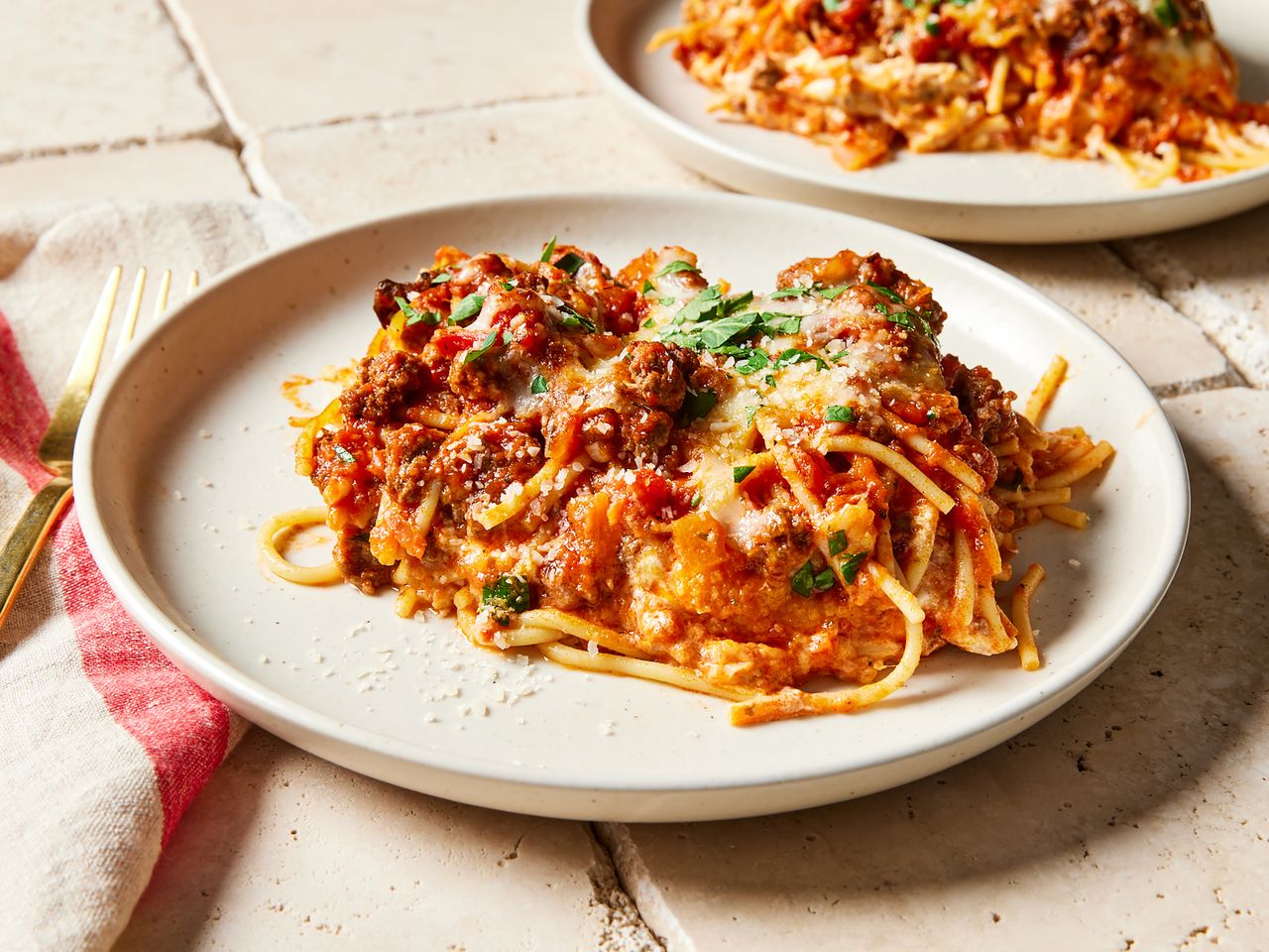 A plate of spaghetti casserole with garnish another plate in the background