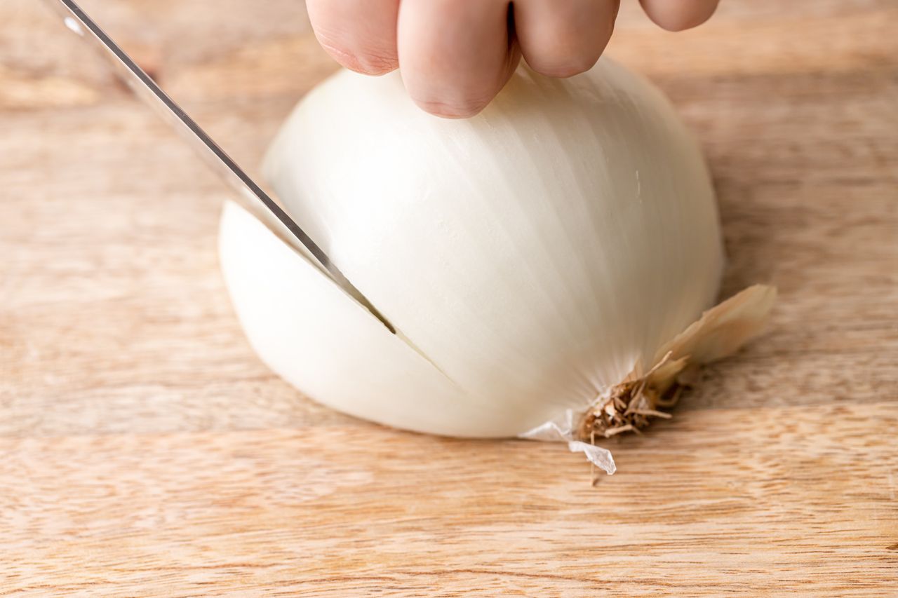 A chef's knife slicing onions for a caramelized onion recipe.