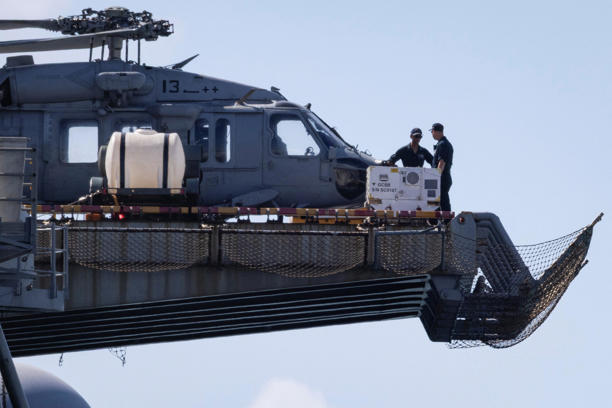 Personnel are seen next to a U.S. Navy MH-60S Knighthawk helicopter sited on the flight deck of the amphibious assault ship USS Iwo Jima (LHD-7) while the vessel is docked in Ponce amid ongoing military movements in Puerto Rico, December 17, 2025.
