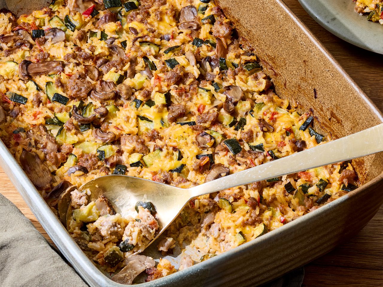 A cheesy sausage and zucchini casserole with a serving spoon in a baking dish