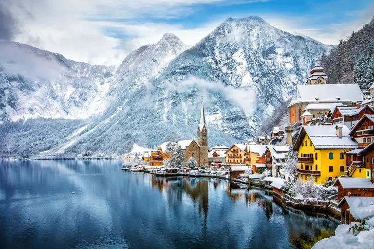 Vista de la ciudad de Hallstatt nevada cuyo centro histórico se estira sobre la estrecha orilla norte de un lago rodeado de montañas surcadas por senderos.