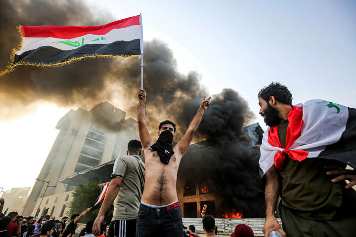 Seorang pemrotes bertopeng mengibarkan bendera nasional Irak selama demonstrasi menentang korupsi negara dan layanan yang buruk, antara ibukota Tahrir Square di Baghdad dan distrik Green Zone. Foto: AFP/AHMAD AL-RUBAYE
