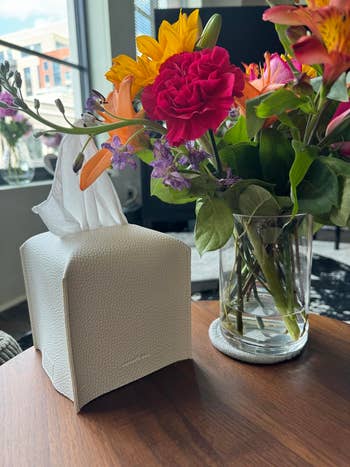 reviewer's white faux leather tissue box cover next to a vase of mixed flowers