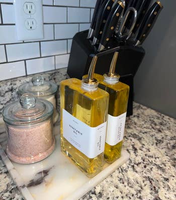 reviewer's kitchen countertop with knife block set, pink Himalayan salt in lidded jars, and two of the narrowm labeled vegetable oil bottles with stainless steel pumps