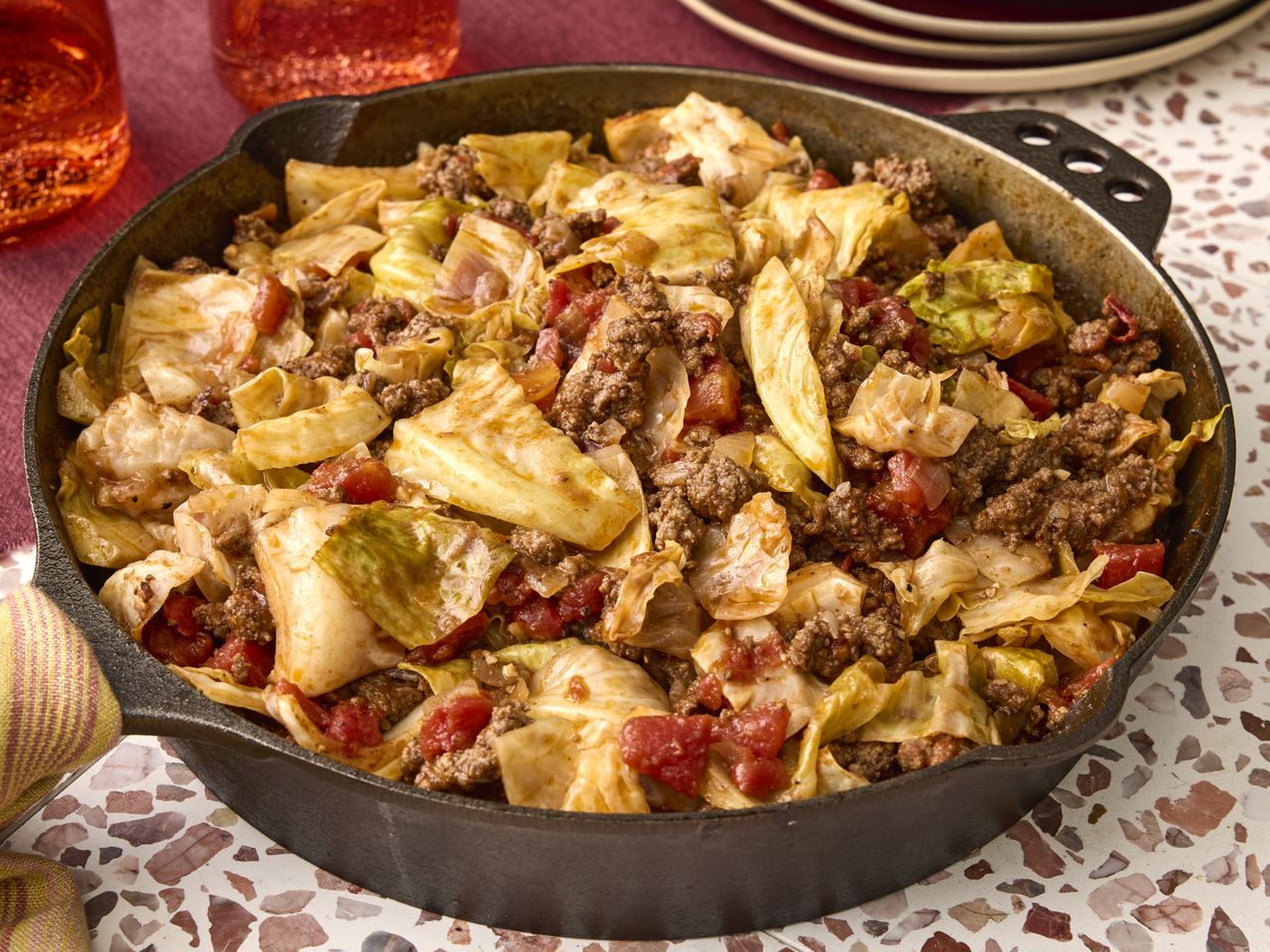 A skillet containing a dish with cooked cabbage ground meat and tomatoes resembling unstuffed cabbage rolls