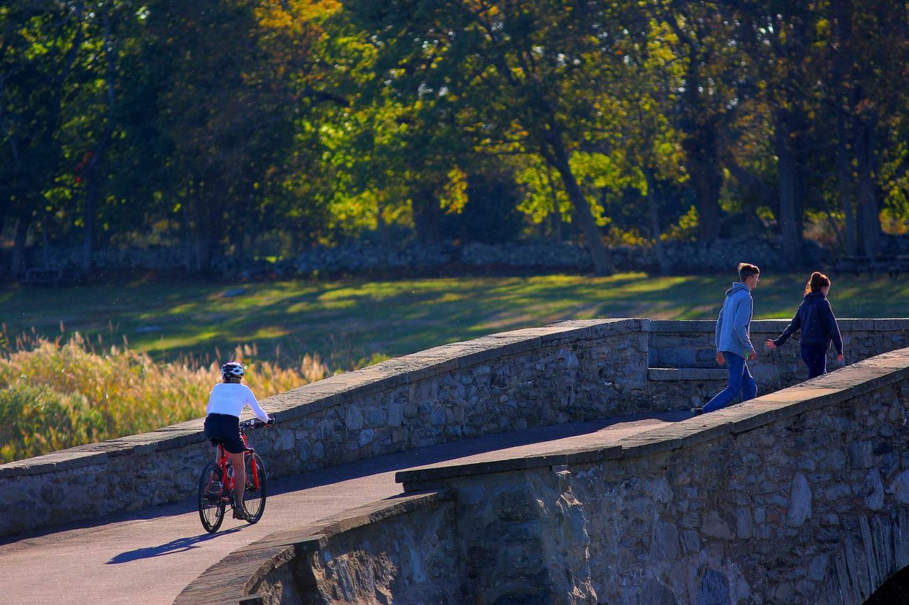Park visitors cross a small bridge over the Mill Gut shellfish management area at Colt State Park in Bristol, Rhode Island