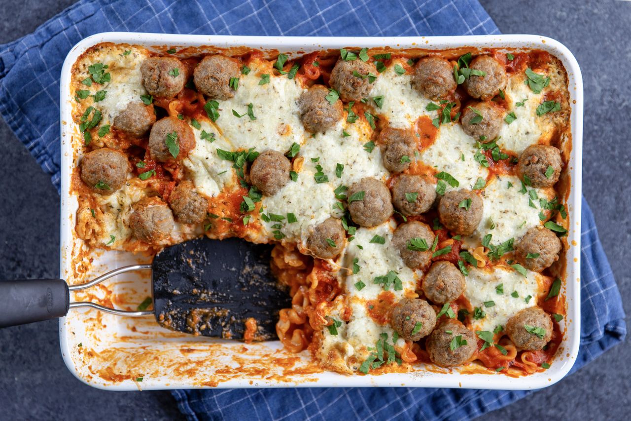 Baked pasta casserole topped with meatballs and cheese a portion removed showing layers of pasta and sauce