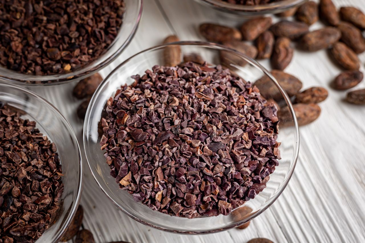 Bowl of cacao nibs surrounded by cacao beans