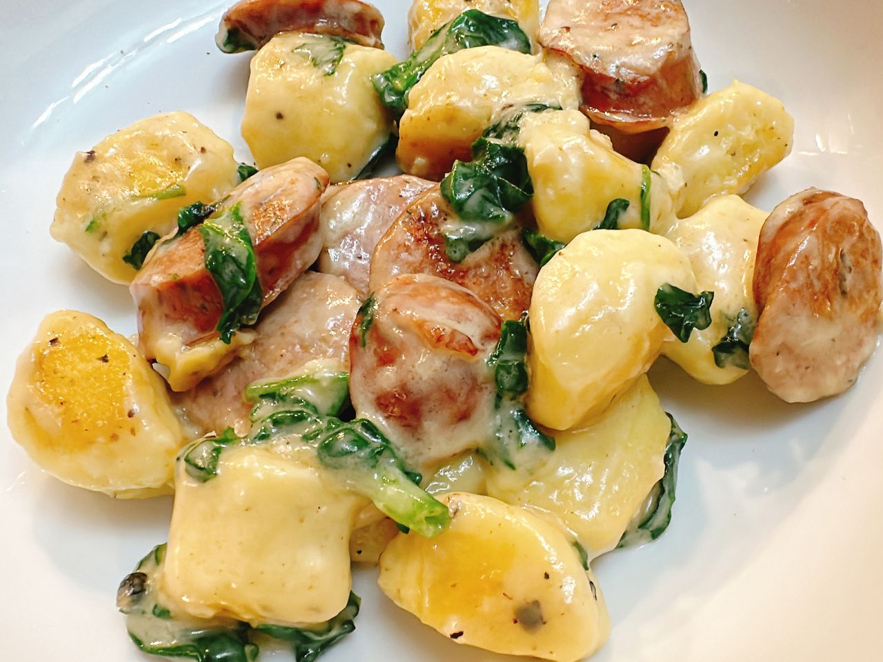 white plate with gnocchi, sausage, and spinach