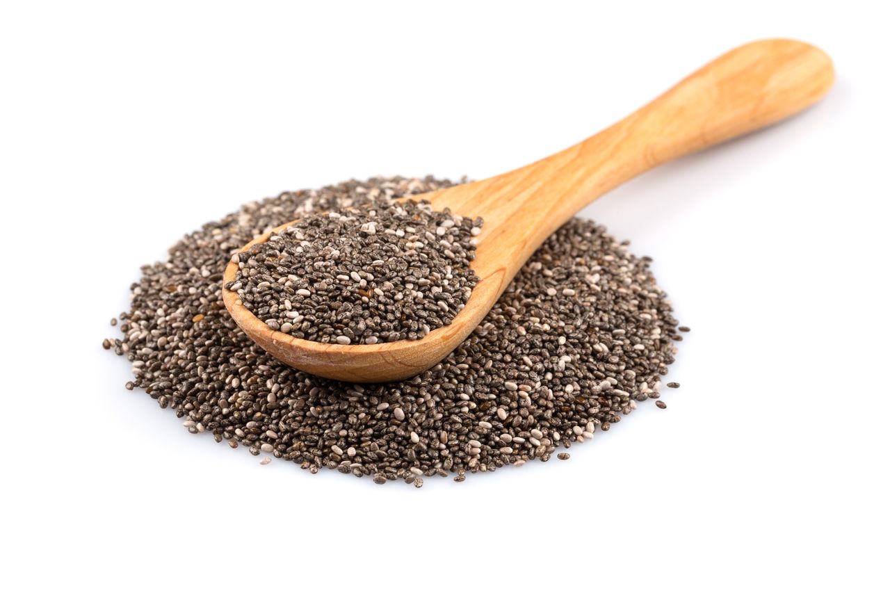 A wooden spoon with chia seeds spilling onto a surface