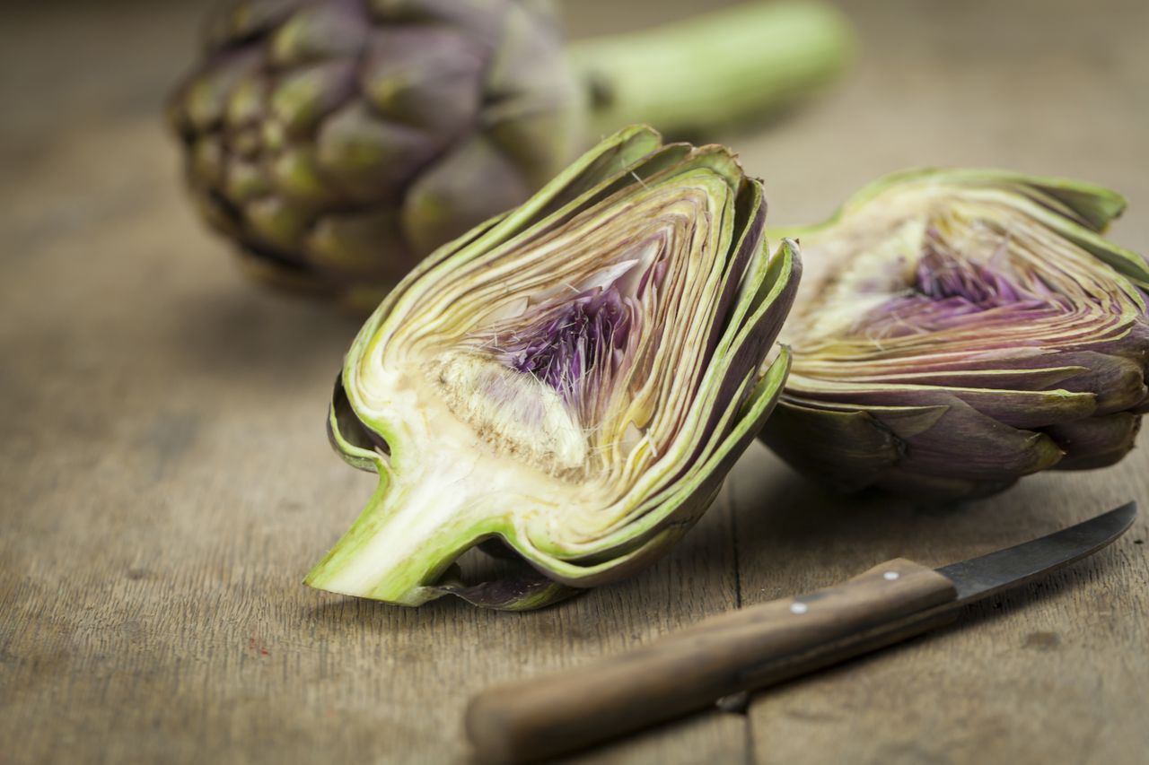 Sliced and whole artichoke on a wooden surface with a knife nearby