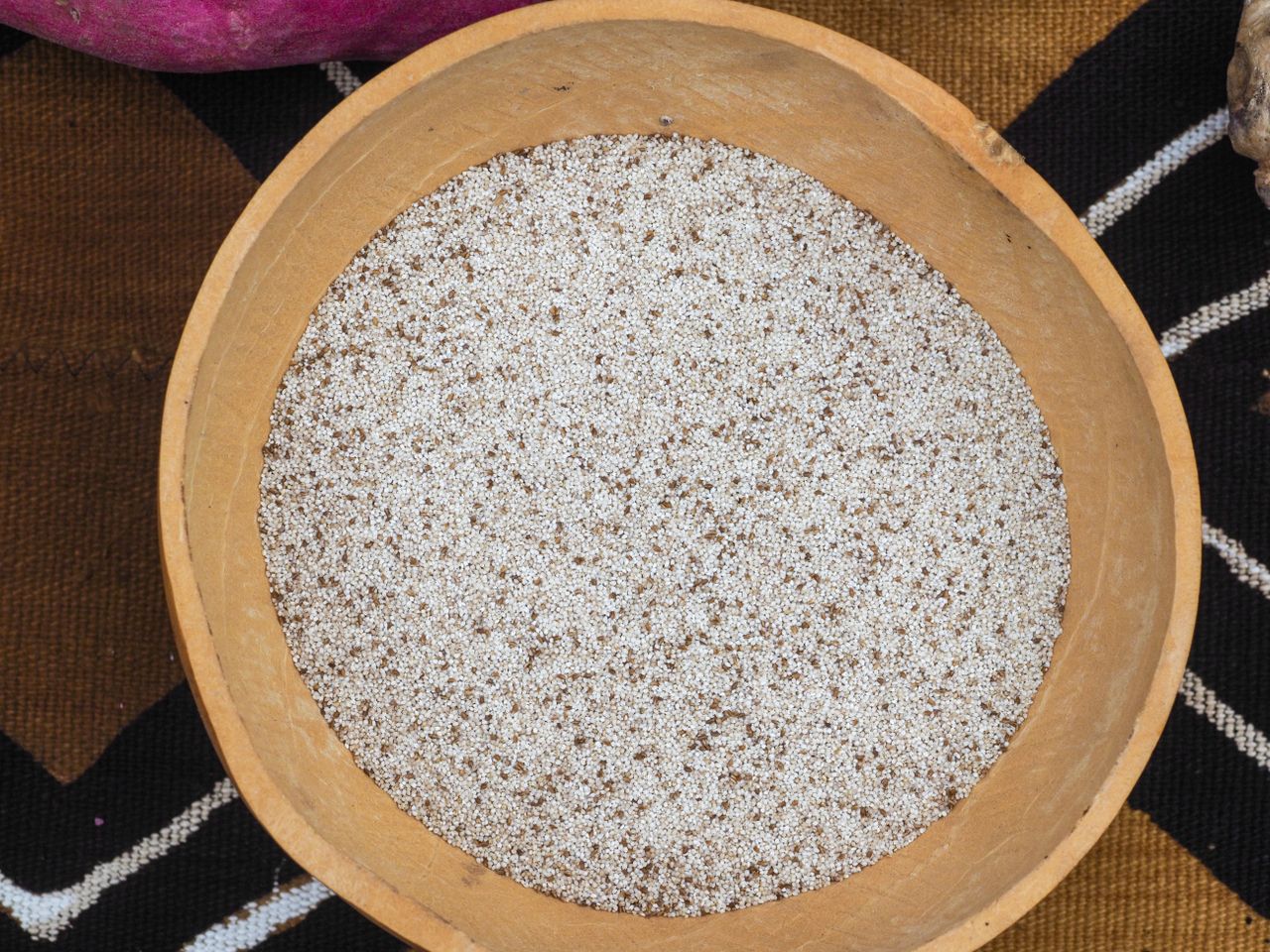 A wooden bowl filled with small white grains resembling a type of cereal or seed