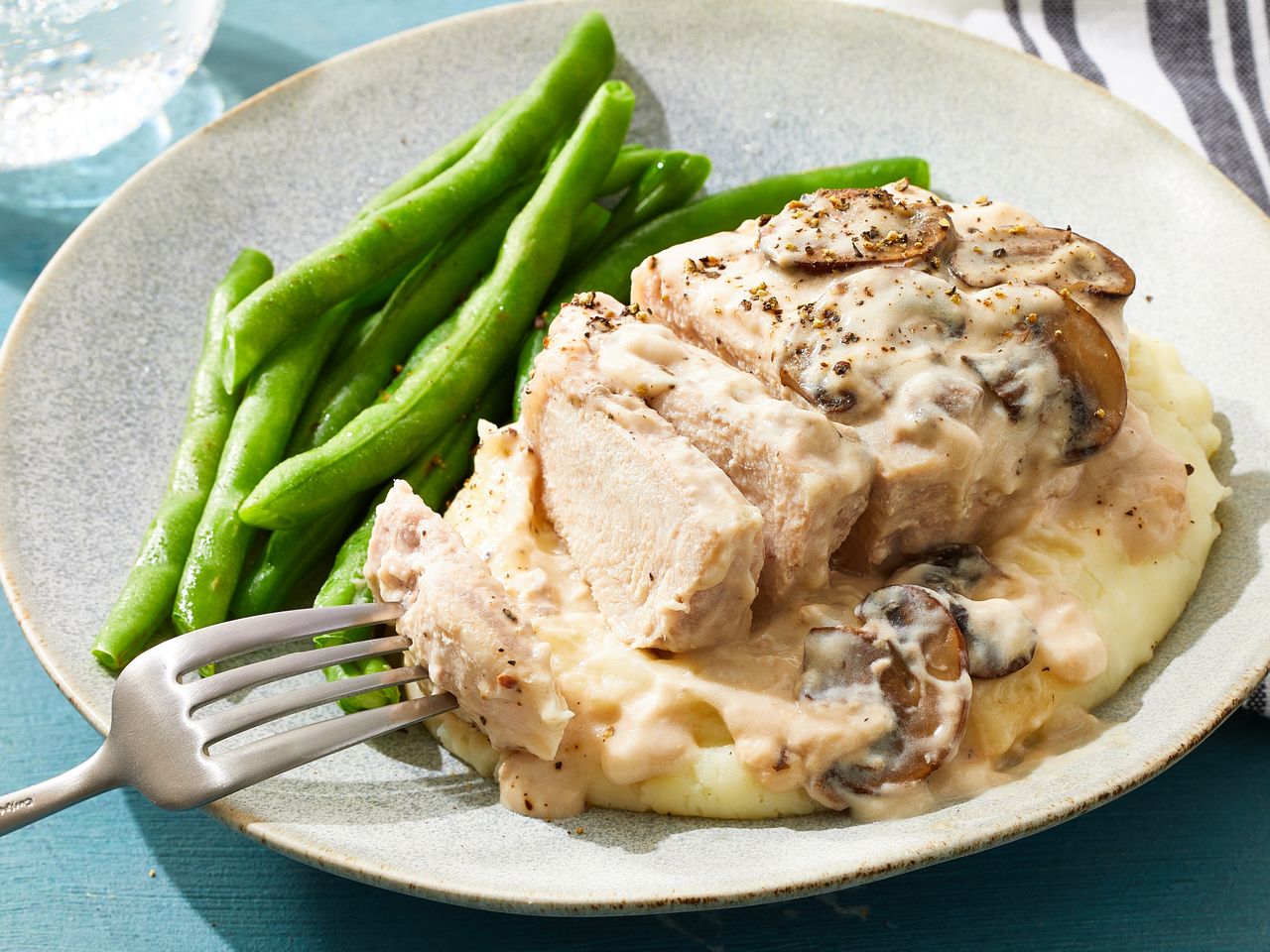 A dish of baked pork chops with cream of mushroom sauce served with green beans and mashed potatoes
