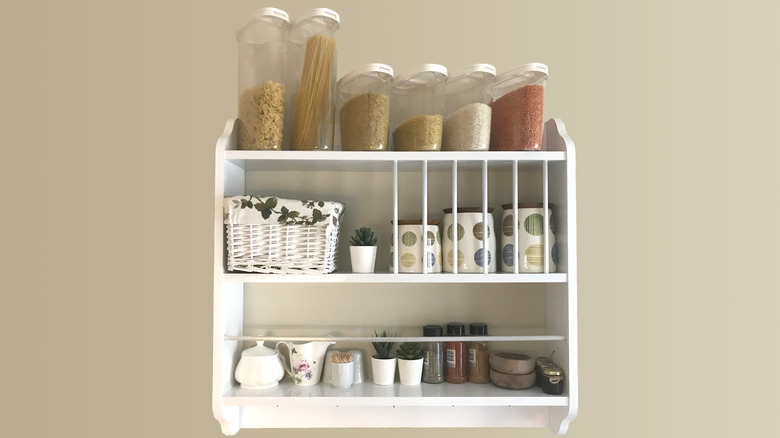 A white wooden spice rack hanging on a wall, holding kitchen pantry items