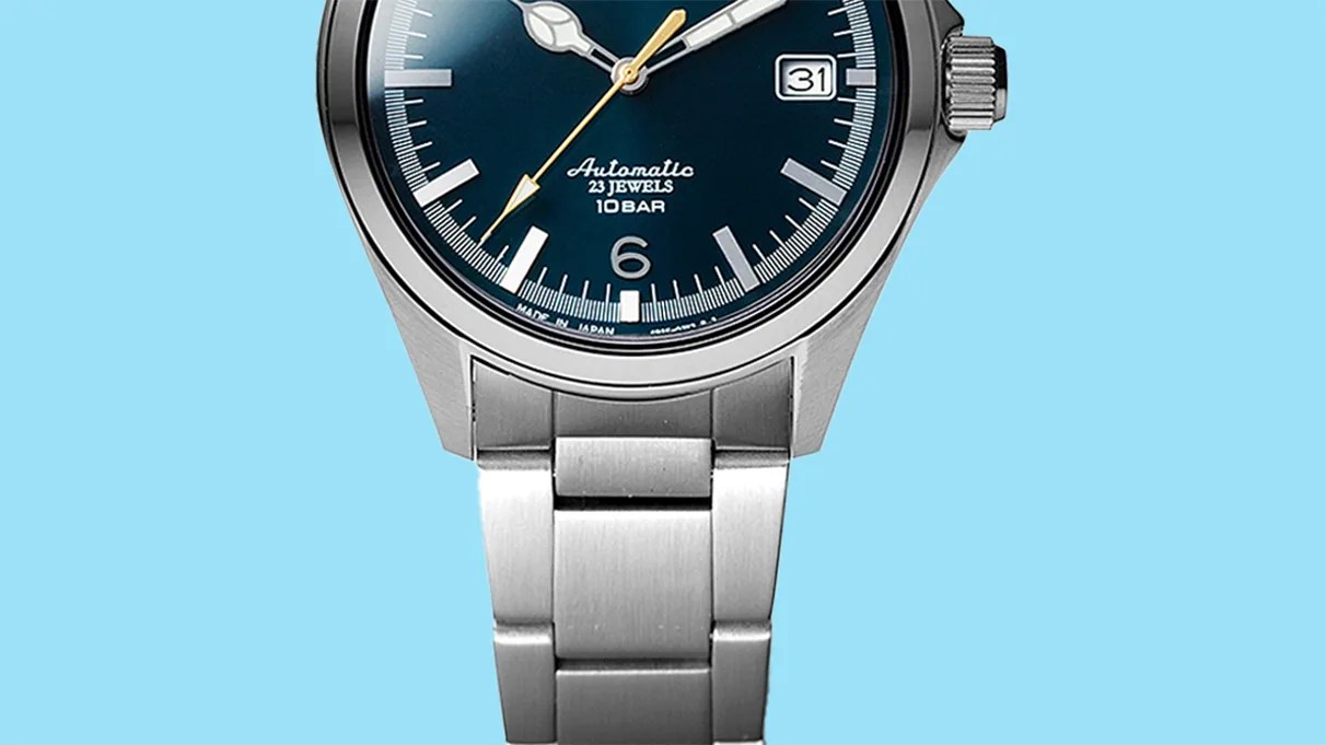 Close-up of a stainless steel wristwatch with a blue dial, silver hour markers, and a date window at 3 o'clock.
