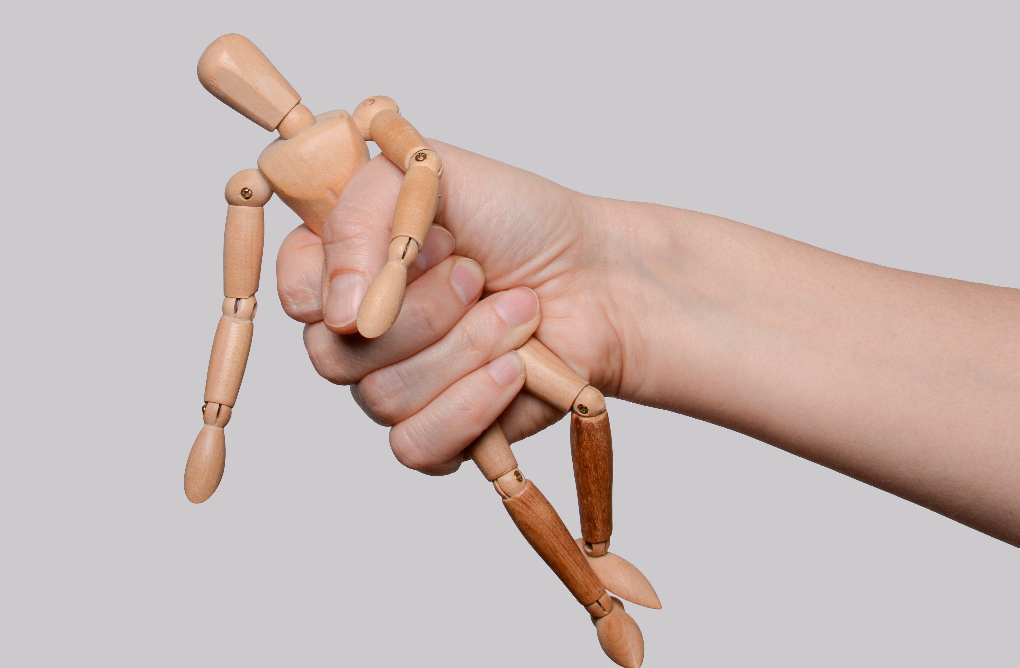 Hand gripping a wooden artist's mannequin by the torso, bending its limbs
