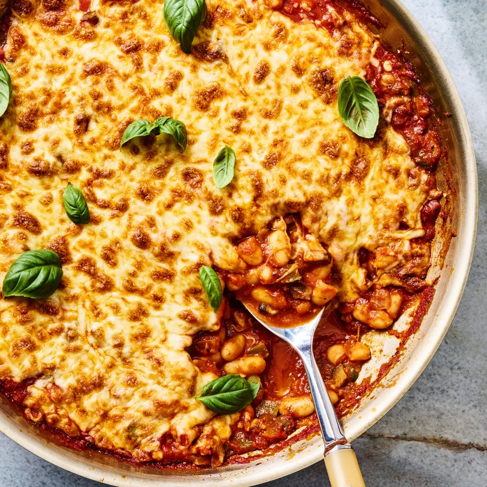 Cheesy baked skillet dish with tomato sauce beans and basil garnish with a serving spoon