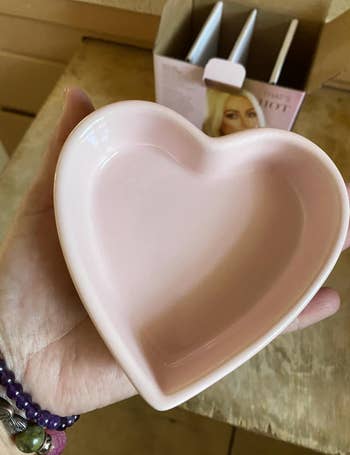 Heart-shaped ceramic dish held in hand, with a cardboard package partially visible in the background