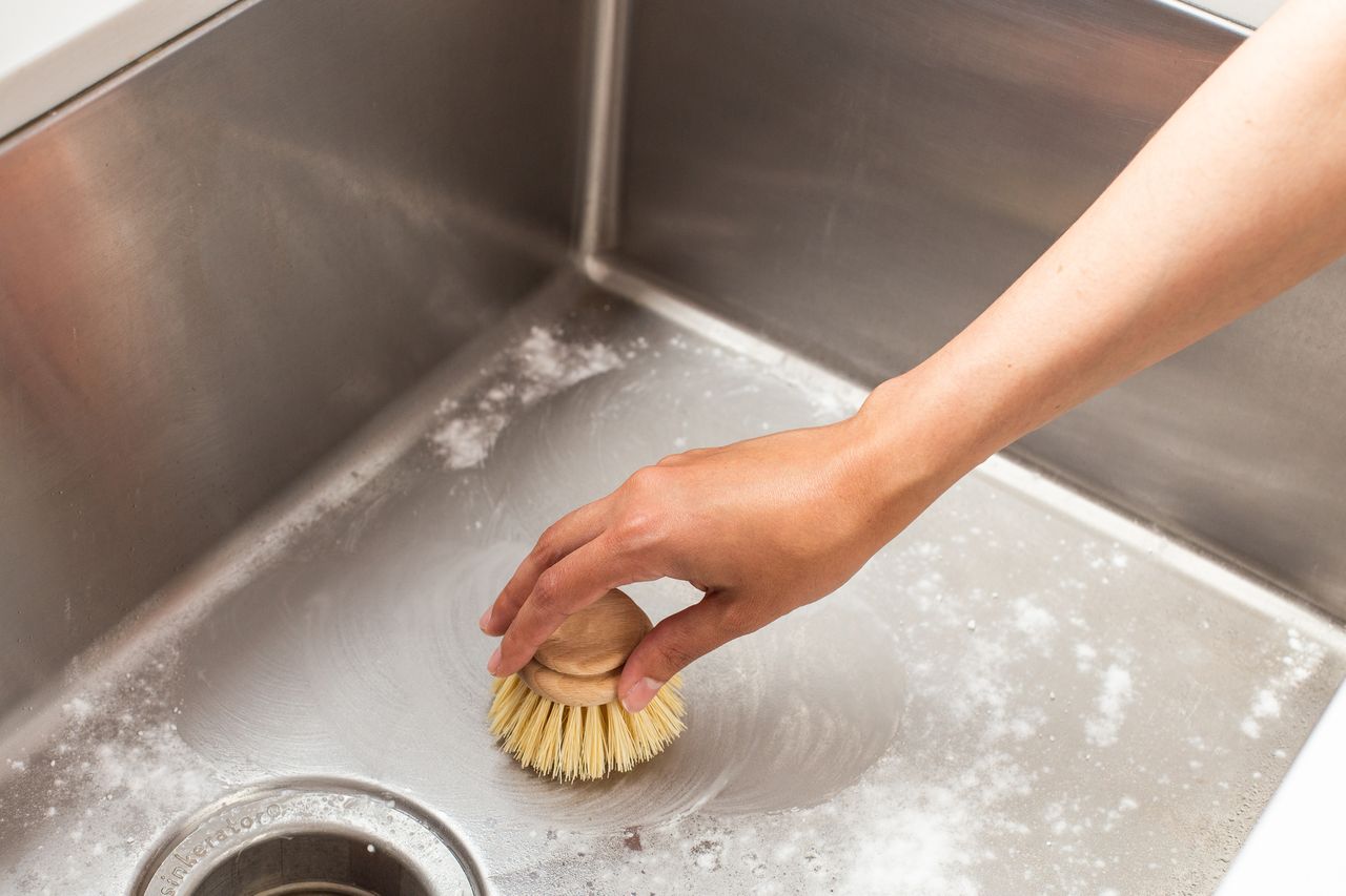 Soft-bristled brush scrubbing stainless steel sink with baking soda