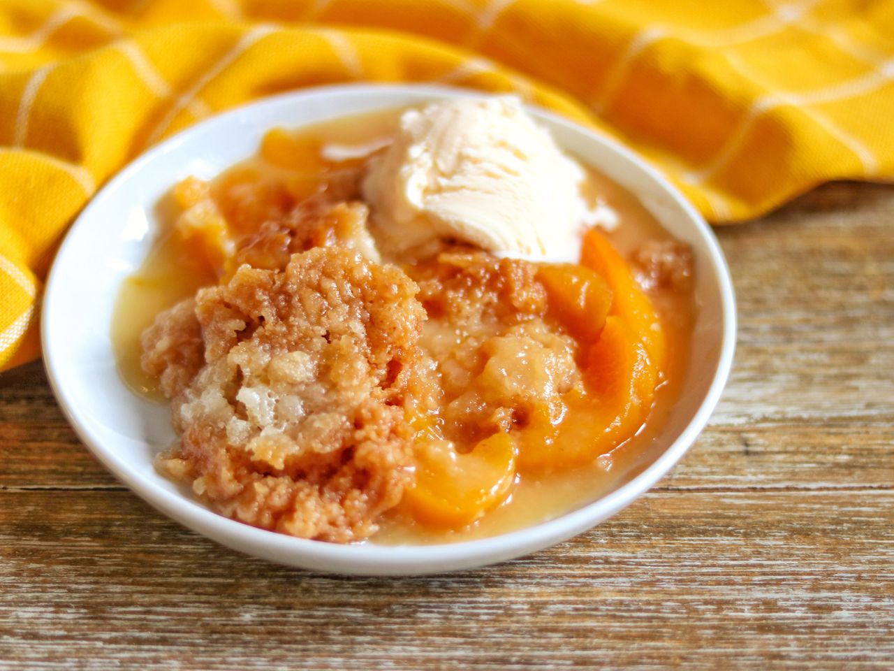 peach cobbler with vanilla ice cream in white bowl